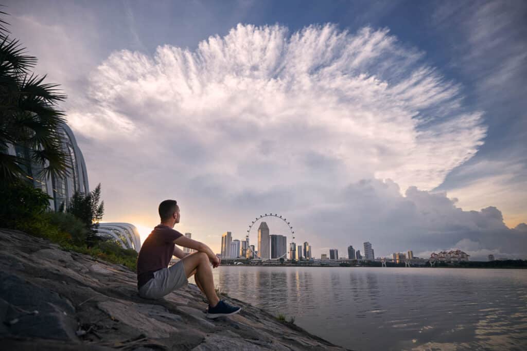 Man sitting on waterfront in Singapore looking at dramatic clouds.