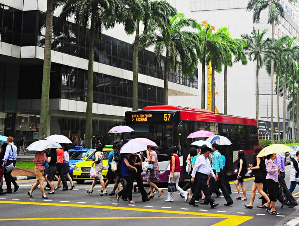 People crossing road with umbrellas in Singapore.