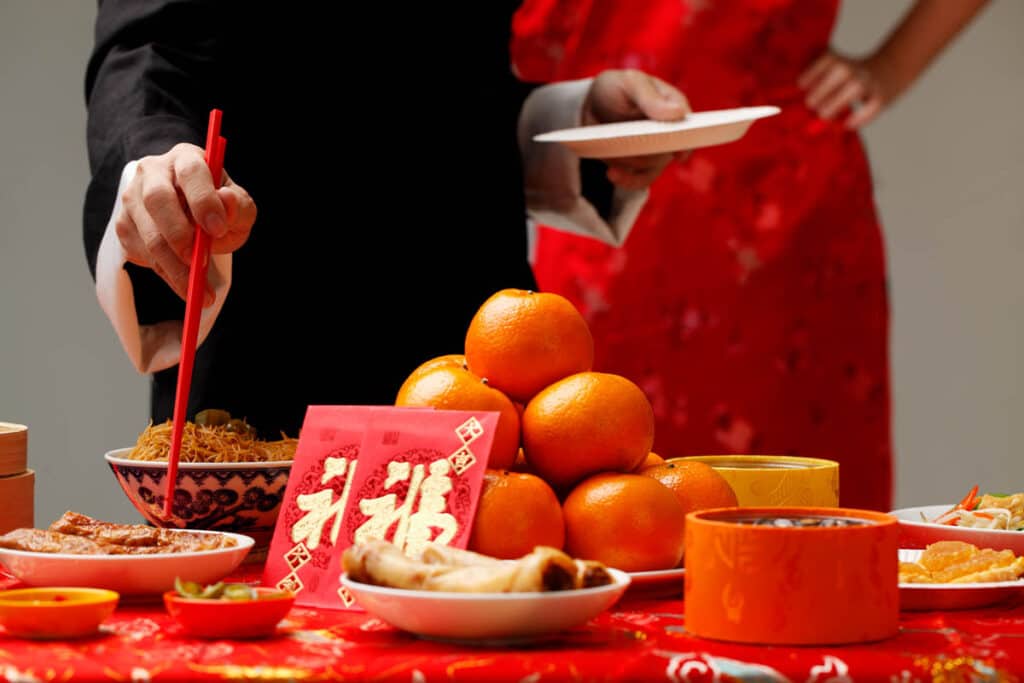 Table laden with Chinese New year food, oranges and hong bao red packets. 