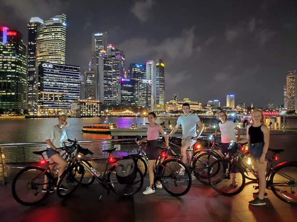 People with bikes at night in Singapore with skyline behind. 
