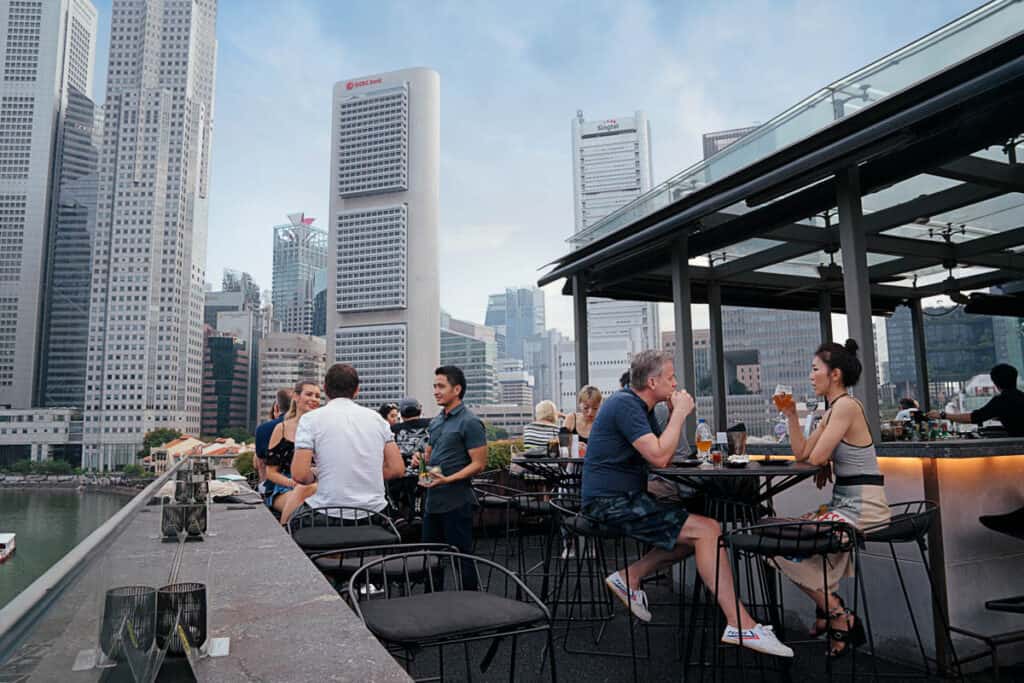 People drinking in bar with Singapore skyline view.