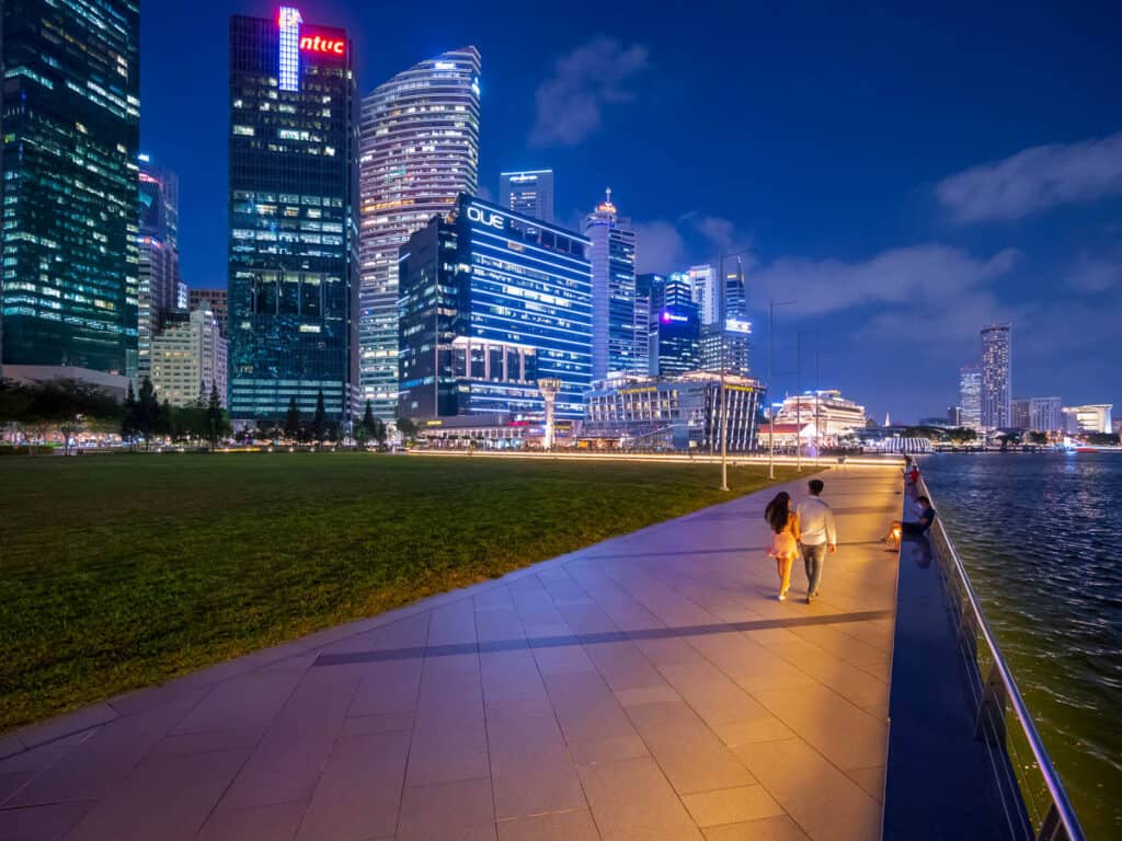 Couple walking with Singapore skyline backdrop at night. 