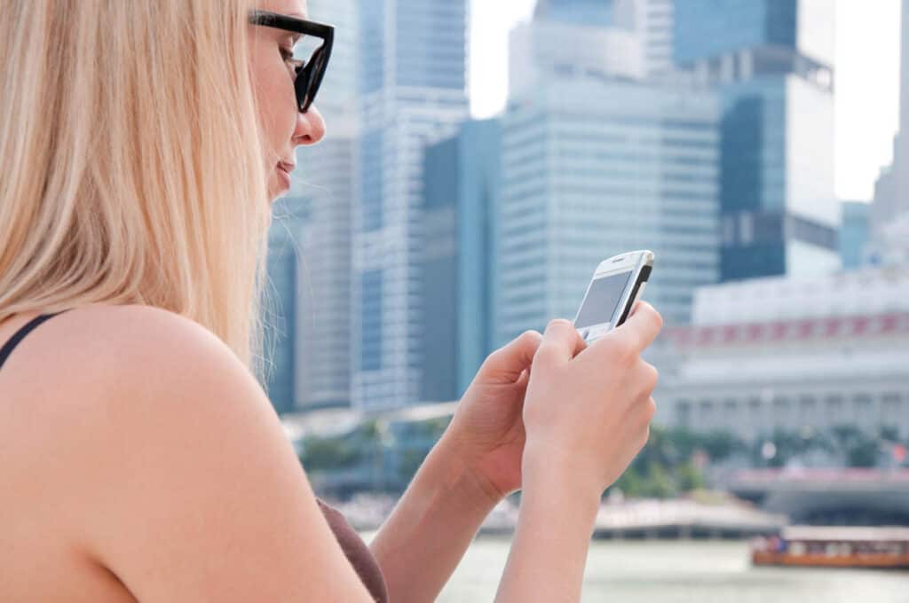 Woman on phone in Singapore with Marina Bay backdrop.