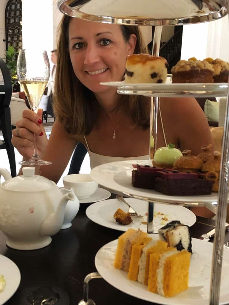 Woman with glass of champagne and three tier stand in foreground. 