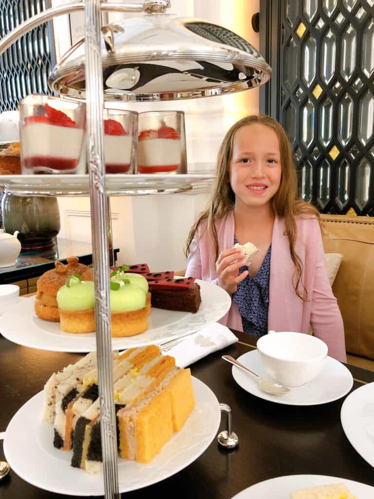 Girl enjoying afternoon tea at Raffles with three tier stand in foreground. 