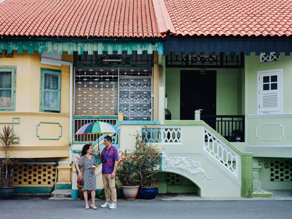Couple standing under an umbrella with traditional Singapore building behind. 